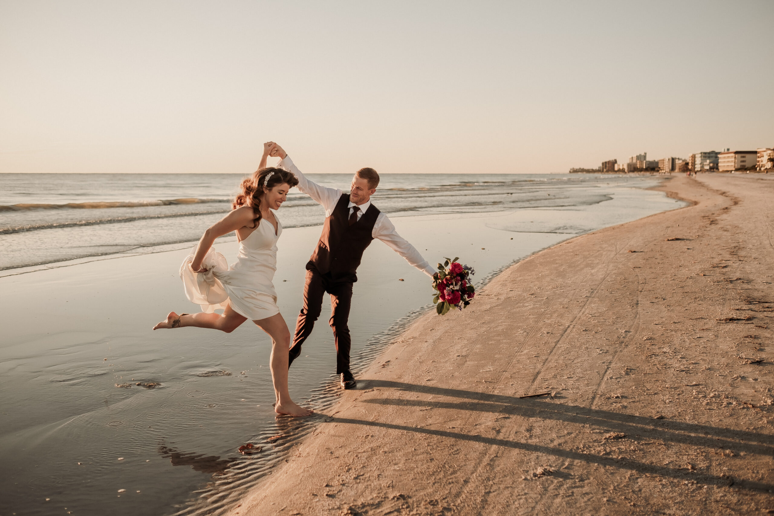 Bride and groom play on the beach for wedding at The West Events captured by Paisley Sunshine, a Madeira Beach wedding photographer.