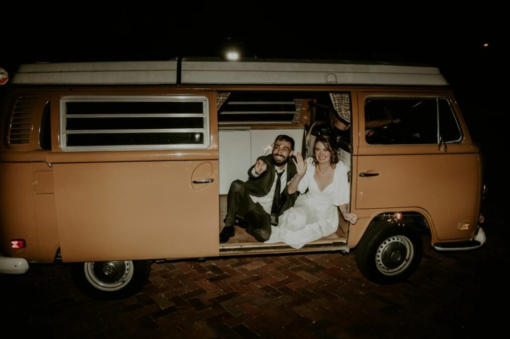 The couple poses with a Vintage Westfalia Volkswagen bus before departing from their wedding reception